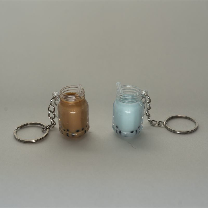 Two bubble tea keychains shaped like tiny jars with straws, one milk tea and one blue